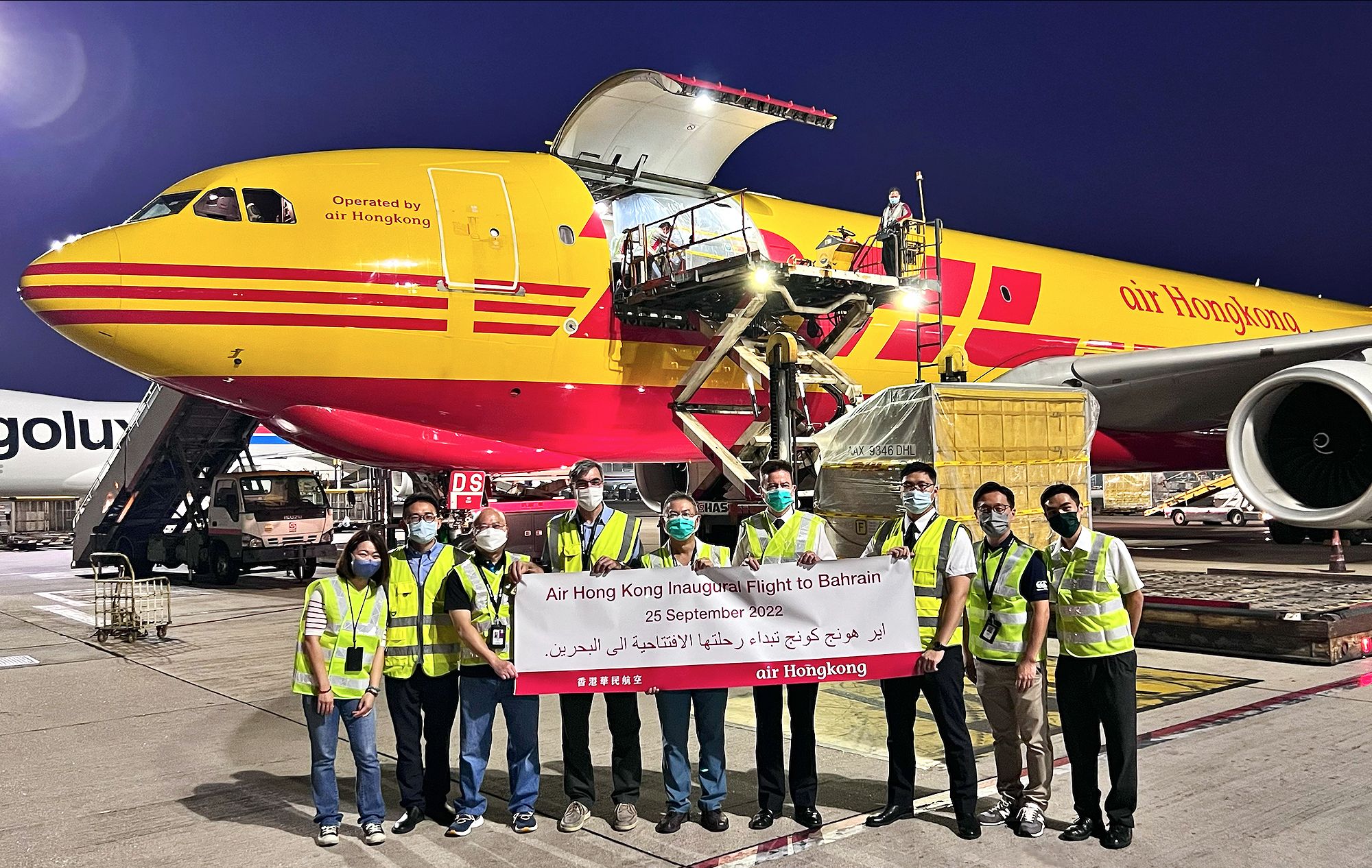 Photo of a group of staff in safety vest holding up a banner in front of an air hong kong and DHL freighter