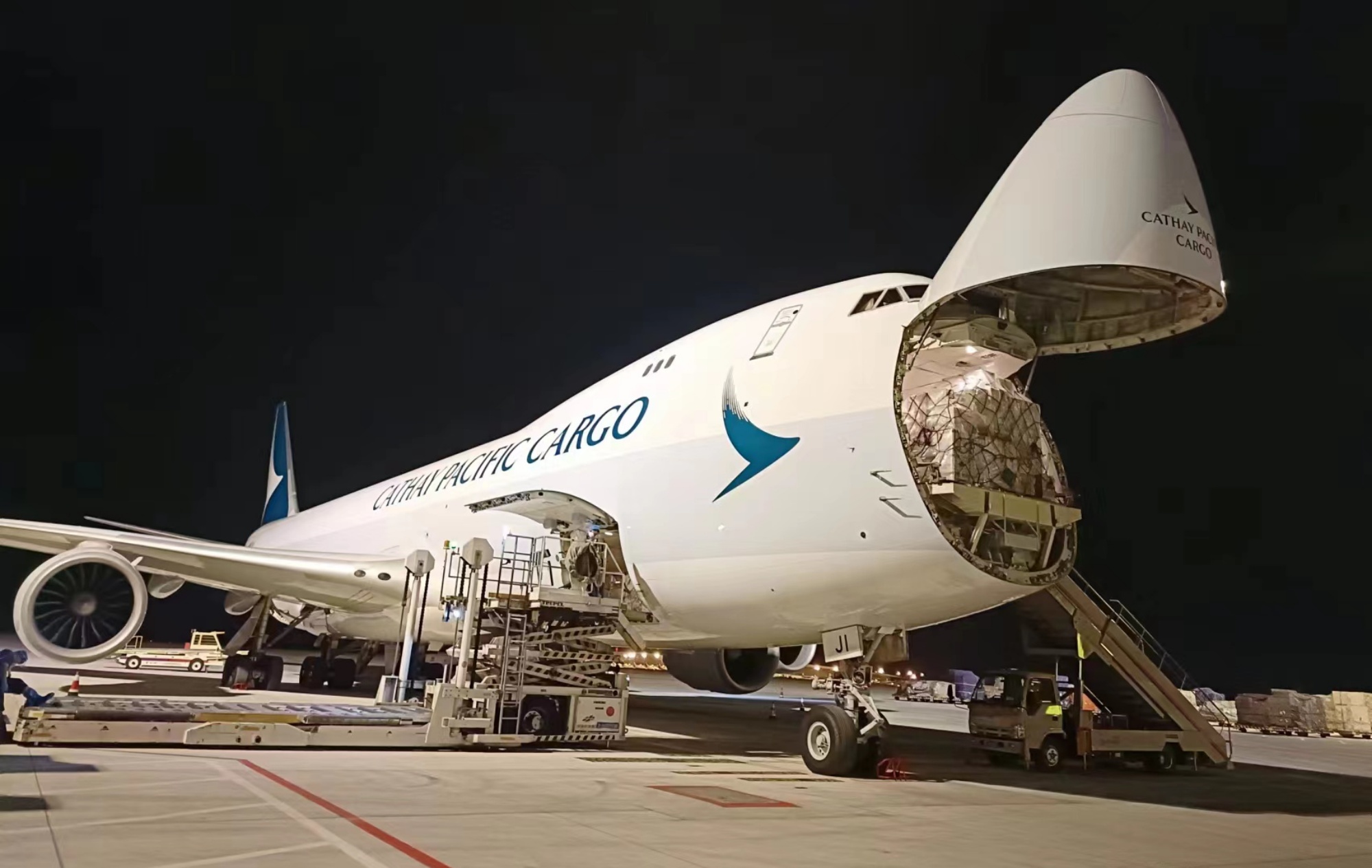 a Cathay Pacific Cargo freighter with its nose opened to load shipments at night
