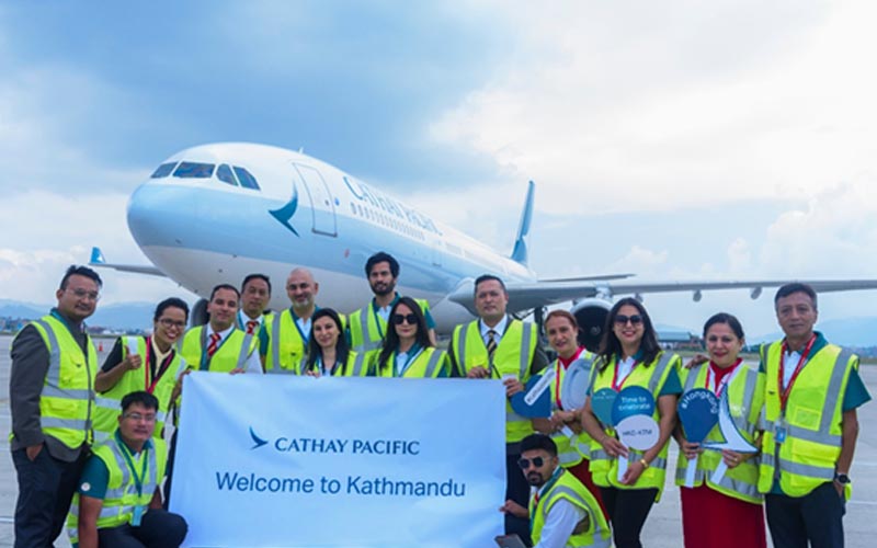 A group of staff stand in front of a Cathay Pacific plane with a Welcome to Kathmandu sign